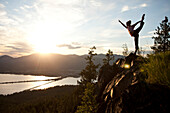 Young woman doing yoga at the top of a mountain overlooking a small town and large lake Sandpoint, Idaho, USA