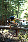 A young man jumps over a fallen tree while hiking in Idaho Priest Lake, Idaho, USA