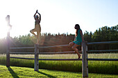 Two young women balancing on a wooden fence next to a green field Sandpoint, Idaho, USA