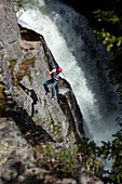 A young man rappels down a cliff next to a waterfall in Idaho Sandpoint, Idaho, USA