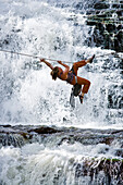 A woman crosses a waterfall using a Tyrolean Traverse on a rope Utah, USA