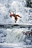 A woman crosses a waterfall using a Tyrolean Traverse on a rope Utah, USA