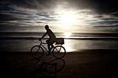 A male rides his bike to work at the beach at sunrise TamandareÌ_, Pernambuco, Brazil