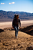 During the heat of the midday sun, a male hiker trudges through Death Valley's Confidence Hills, California Death Valley, California, United States of America