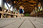 A little girl runs across a covered bridge Newry, Maine, USA