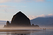 A family and other people walk on Cannon Beach in front of Haystack Rock, Oregon Coast Cannon Beach, Oregon, USA