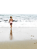 young girl runs to the ocean in southern maine, maine, usa