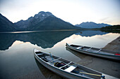 Two canoes at dusk are beached on the shore of Lake Leigh with the Grand Tetons in the distance Jackson Hole, Wyoming, U.S.A.