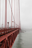 A small sailboat passes under the Golden Gate Bridge on a foggy day in San Francisco, California San Francisco, California, USA