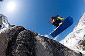A boy snowboarding off a rock in the California backcountry Sierra, CA, USA