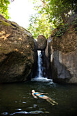 A woman floats on her back while swimming in a pool of water with a waterfall Ojochal, Costa Rica