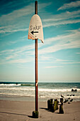 A sign points to the surf at a beach New York, USA