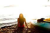A beautiful young woman relaxes on a beach after kayaking at sunset on a lake in Idaho Sandpoint, Idaho, USA