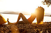 A beautiful young woman relaxes on a beach after kayaking at sunset on a lake in Idaho Sandpoint, Idaho, USA