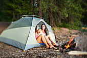 Two beautiful women laugh and smile sitting in their tent next to a campfire in Idaho Sandpoint, Idaho, USA
