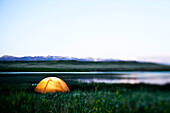 A glowing tent next to a lake at sunset in Montana Bozeman, Montana, USA