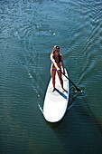 A athletic women smiling on a sunny day while stand up paddle boarding on a lake in Idaho., Sandpoint, Idaho, USA