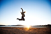 A athletic young woman leaping into the air at sunset next to a lake in Idaho., Sandpoint, Idaho, USA