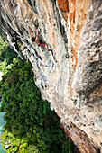 A athletic man rock climbing high above the trees and water on a multi pitch route in Thailand., Railay, Thailand