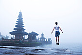 A man leaping into the air on the steps of a temple with a foggy background in Bali, Indonesia., Ulun Dabu Beratan Temple, Bali, Indonesia