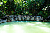 A beautiful woman relaxing next to a hot springs surrounded by a lush jungle and flowers in Bali, Indonesia., Lovina, Bali, Indonesia