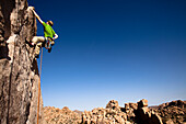 A male climber in a green shirt climbs Sail Away (5.8) in The Real Hidden Valley of Joshua Tree National Park, California., Joshua Tree, California, United States of America