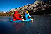 Two male ice climbers using ice axes row their way across Tenaya Lake in Yosemite, California., Yosemite, California, United States of America