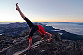 A woman performs yoga on the summit of Mount Tallac with Lake Tahoe in the background at sunset, CA., Lake Tahoe, California, USA
