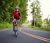 A female cyclist rides on a rural country road in New England., Whately, MA, USA