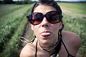 A young woman wearing sunglasses sticks her tongue out at the camera on a warm summer day., Hatfield, MA, USA