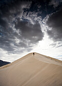 A man walks on natural sand dunes beneath a cloudy sky in Mojave Desert, California Mojave National Preserve, California, USA