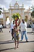 Pilger trägt heiliges Wasser auf dem Kopf, Tor zum Amba Vilas Palast im Hintergrund, Mysore, Karnataka, Indien