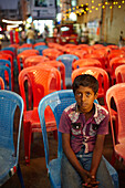 Boy sitting on chair in front of a stage, Mysore, Karnataka, India