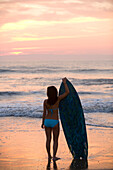 Asian girl holding surfboard at beach, Virginia Beach, VA
