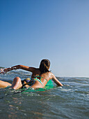 Hispanic girl paddling on surfboard, Newport Beach, CA