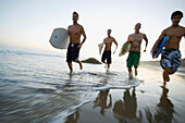 Multi-ethnic men running with surfboards, Newport Beach, CA