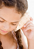 Hispanic girl listening to seashell, Rockaway Beach, NY