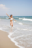 Hispanic girl running in waves at beach, Rockaway Beach, NY