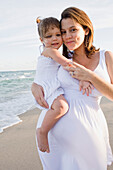 Pregnant mother holding daughter at beach, Fort Lauderdale, FL