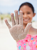 Hispanic girl displaying sand-covered hand, Rockaway Beach, NY