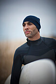 African American man in wet suit carrying surfboard, Virginia Beach, VA