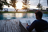 Caucasian man reading at poolside, Kep, Kep, Cambodia