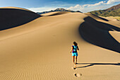 Hispanic woman running on sand dune, Great Sand Dunes National Park, Colorado, USA