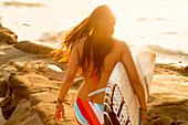 Mixed race woman carrying surfboard on beach, San Diego, CA, USA