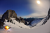 Woman in front of an illuminated tent near mount Risserkogel, Plankenstein in background, Bavarian Prealps, Upper Bavaria, Germany