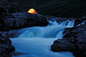 Illuminated tent beside a river, Glen Etive, Highlands, Scotland, Great Britain