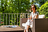 Frau mit Weinglas sitzt auf einem Balkon mit Loungemöbeln, Hamburg, Deutschland