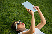 Mittlere erwachsene Frau liegt im Park und benutzt ein digitales Tablet