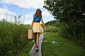 Teenage girl carrying suitcase on rural path