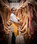Portrait of Italian butcher surrounded by hanging pig carcasses